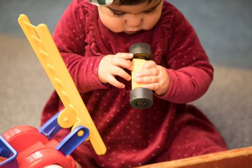 Ein Kind sitzt auf dem Boden und spielt mit Holzspielzeug.